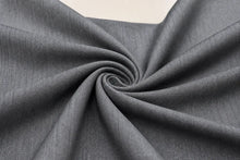 A close-up of dark gray textured fabric arranged in a spiral drape, showing the material's fine woven pattern and soft folds.