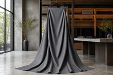 A dark gray ribbed knit fabric, likely a scarf or long wrap, draped elegantly from a hanger in a modern, minimalist interior room with concrete floors and wooden shelving.