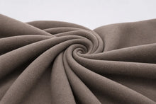 A close-up of draped taupe-brown fabric arranged in a spiral swirl, showing its soft texture and folds against a light neutral background.
