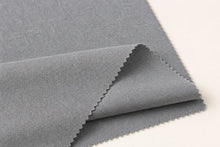 A close-up of a folded piece of medium gray woven fabric with a textured, linen-like surface, showing serrated edges, set against a plain off-white background.