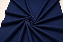 A close-up of dark navy blue fabric arranged in a spiral drape pattern against a light off-white background.