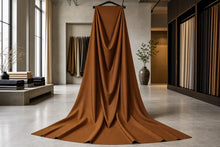 A large draped piece of rust-brown fabric hangs from a black hanger in a modern, minimalist interior showroom with concrete floors and neutral-toned walls.
