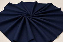 A dark navy blue fabric, likely a skirt or scarf, arranged in a neat spiral pattern on a light beige background.