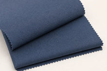 Two folded pieces of textured blue fabric with serrated edges, stacked on a plain white background.