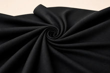 Black fabric draped in a spiral swirl pattern, showing its fine woven texture against a light beige background.
