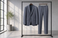 A gray two-piece suit, consisting of a blazer and matching trousers, displayed on a black clothing rack in a bright, modern room with a window and a potted plant.