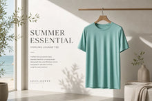 A mint green short-sleeve cooling lounge tee hanging on a wooden hanger from a clothing rack, set in a bright, modern room with a window, text overlay reading 'SUMMER ESSENTIAL COOLING LOUNGE TEE', and decorative plants.