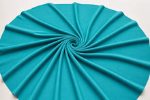 A bright turquoise blue fabric, likely jersey or cotton, draped in a neat spiral pattern on a plain white background.