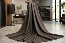 A long, draped brown knit fabric or sweater skirt with a wide flared hem, hanging from a wooden hanger in a modern, stylishly decorated room.