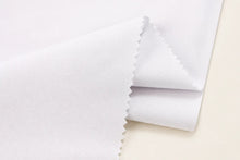 A close-up of folded white fabric with serrated edges, showing a smooth woven texture on a light neutral background.
