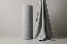 Roll of gray textured fabric next to a draped piece of gray textured fabric on a neutral background